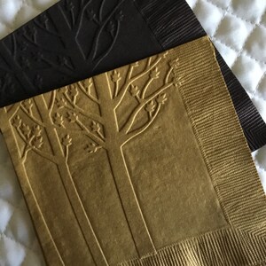 May include: Two paper napkins with an embossed tree design. One napkin is gold and the other is black.