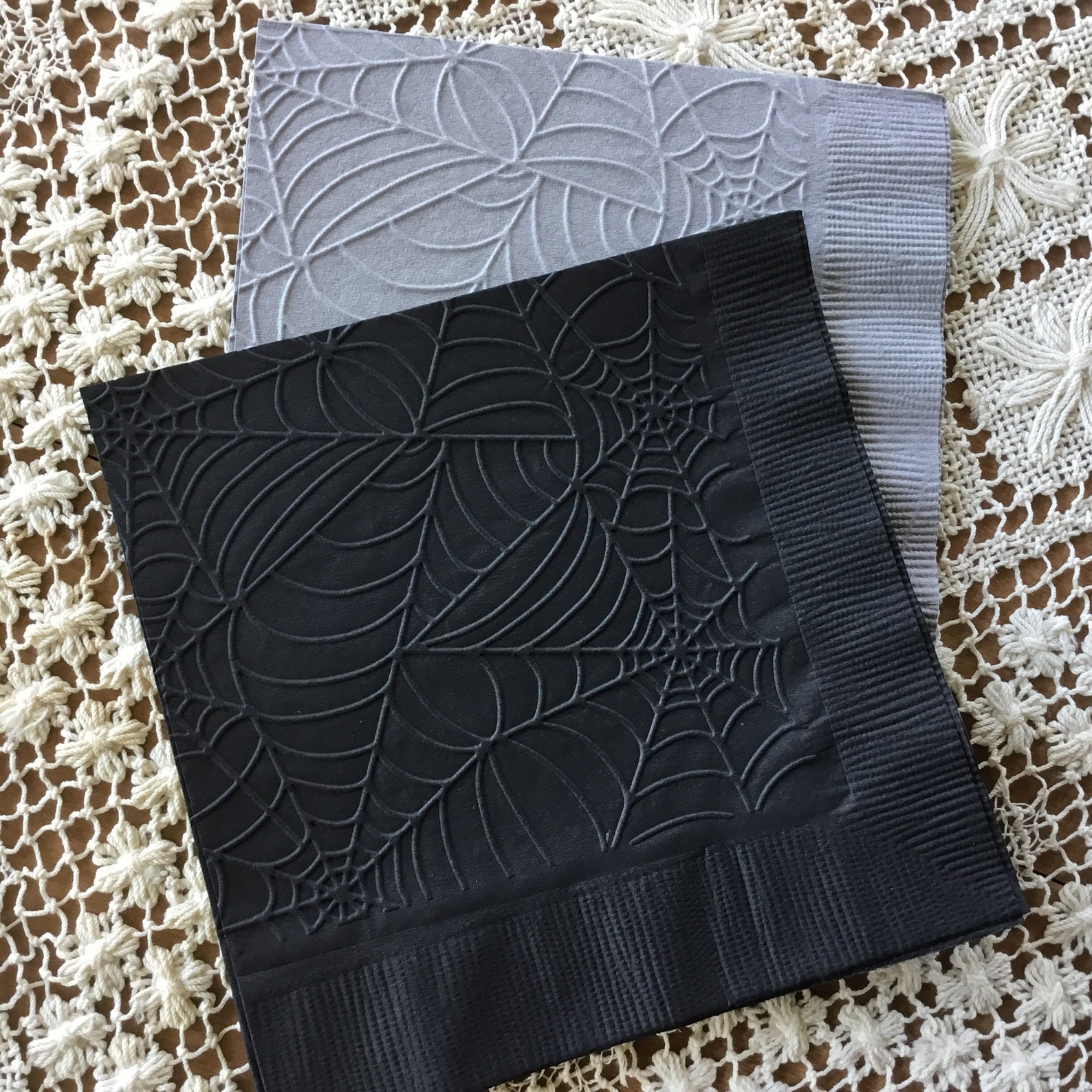 An Embossed Web Instead of an Added Ring Dark paper napkins with a raised spiderweb pattern.