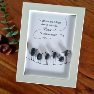 Può includere: Una cornice bianca con un disegno in bianco e nero di uccelli fatti di piccole pietre grigie. Il testo nella cornice dice "Es gibt viele gute Kollegen aber wir hatten den Besten! Du wirst uns fehlen!"
