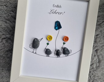 May include: A framed artwork featuring a blue gemstone, four small gray stones painted to look like birds, and the text "Endlich Lehrer!" in black lettering.