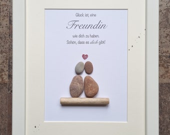 May include: A white framed picture with a white background. The picture features a stone sculpture of two people sitting on a wooden log. The sculpture is surrounded by small black stars. The text in the picture reads "Glück ist, eine Freundin wie dich zu haben. Schön, dass es dich gibt!"