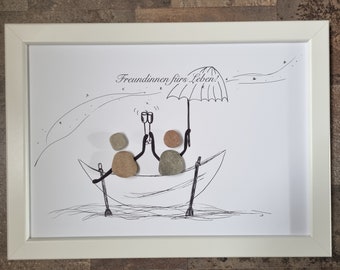 May include: A framed drawing of two figures in a boat with an umbrella above them. The figures are made of stones and are holding up glasses. The drawing is titled "Freundinnen fürs Leben!" which translates to "Friends for Life!"