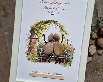 May include: A white framed picture with a watercolor illustration of two stone figures sitting on a bench under a tree. The text reads "Alles Liebe zur Rosenhochzeit Maria & Dieter 20.09.2024 10 Jahre 120 Monate 521 Wochen".