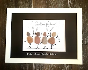 May include: Framed artwork featuring a group of friends depicted with stones, celebrating with champagne. The text "Freundinnen fürs leben!" is above the figures, with names Mila, Anna, Sarah, and Kathrin below. The artwork is framed in white.