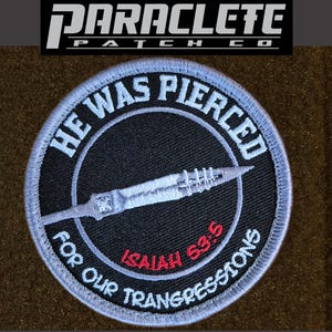 May include: A circular embroidered patch with a black background and a light blue border. The text HE WAS PIERCED FOR OUR TRANSGRESSIONS is stitched in light blue. A light blue spear graphic is centered, with the red text ISAIAH 53:5 below it.