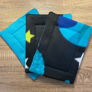 May include: Three fleece fabric squares with different patterns. The top square is blue with white stars, the middle square is black with blue and white circles, and the bottom square is black with blue and yellow stars.