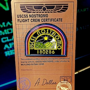 Puede incluir: Un certificado de tripulación de vuelo USCSS Nostromo marrón con un emblema colorido. El emblema presenta la palabra "NOSTROMO" en amarillo, un planeta y el texto "USCSS NOSTROMO". El certificado incluye la fecha "JUN 12 2121" y el nombre "A. Dallas".