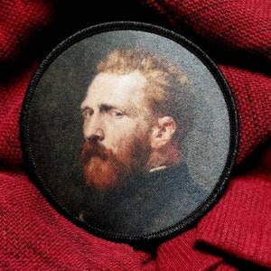 Può includere: Una toppa ricamata in bianco e nero con un ritratto di un uomo con la barba su uno sfondo scuro.
