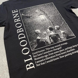May include: Black t-shirt with a white graphic print of a scene from the video game Bloodborne. The text "Good hunter. This may sound strange, But have I somehow changed? Moments ago, from some place, perhaps deep I sensed a liberation from heavy shackles. Not that I would know. How passing strange" is printed below the graphic.