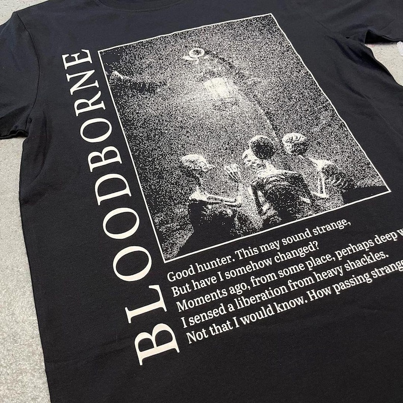 May include: Black t-shirt with a white graphic print of a scene from the video game Bloodborne. The text "Good hunter. This may sound strange, But have I somehow changed? Moments ago, from some place, perhaps deep I sensed a liberation from heavy shackles. Not that I would know. How passing strange" is printed below the graphic.
