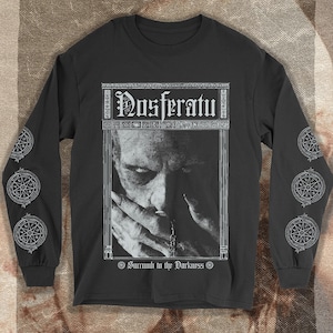 May include: Black long-sleeve shirt featuring a grayscale image of a person with the word "Nosferatu" above the image and "Succumb to the Darkness" below. The sleeves have white circular designs.