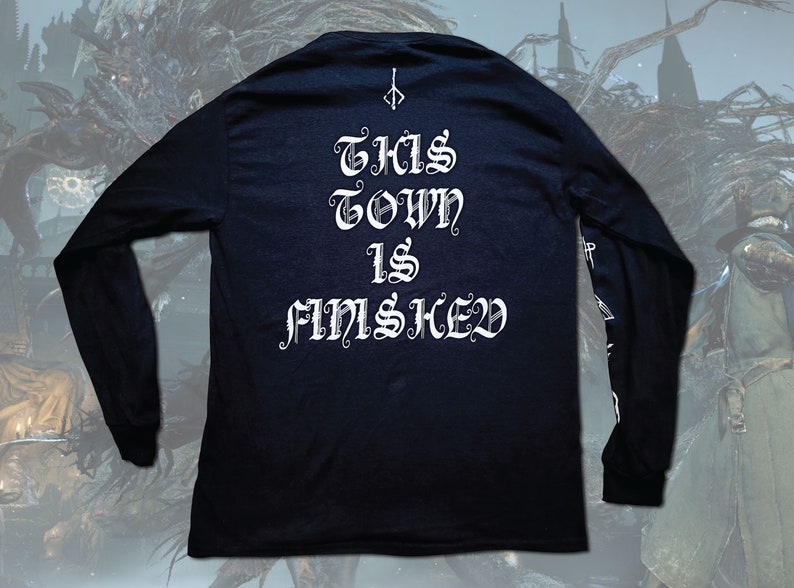 May include: Black long-sleeve shirt with white text that reads "THIS TOWN IS F*MSHED" in a gothic font. The shirt has a small symbol on the top center of the back.