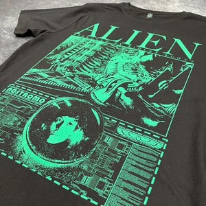 May include: Black t-shirt with a green graphic print of the alien from the movie "Alien" directed by Ridley Scott. The graphic includes the text "Alien" and "Nostromo".