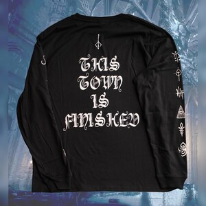 May include: Black long-sleeve shirt with white text that reads "THIS TOWN IS FINSICHED" and white graphic designs on the sleeves.