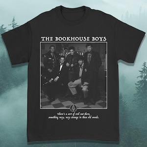 May include: Black t-shirt with a black and white photograph of a group of men. The text "THE BOOKHOUSE BOYS" is above the image. Below the image is the text "There's a sort of evil out there, something very, very strange in these old woods."