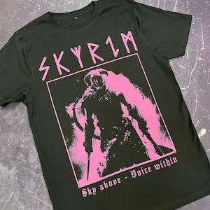 Op de afbeelding: Zwart T-shirt met een roze afbeelding van een personage uit het videospel Skyrim. De afbeelding bevat de tekst "Skyrim" en "Sky above - Voice within".