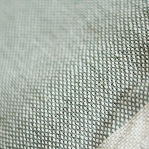 May include: A close-up of a soft, textured fabric with a subtle green and white pattern. The fabric has a woven appearance and a slightly rough texture.