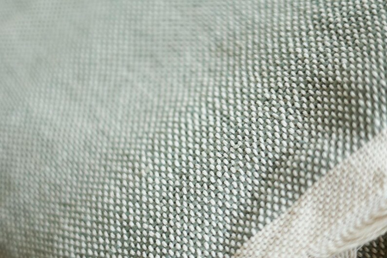 May include: A close-up of a soft, textured fabric with a subtle green and white pattern. The fabric has a woven appearance and a slightly rough texture.