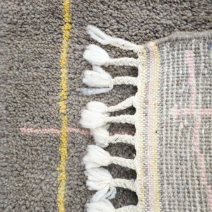 May include: Close-up of a gray and white woven rug with a fringe border. The rug has a geometric pattern with yellow and pink accents.