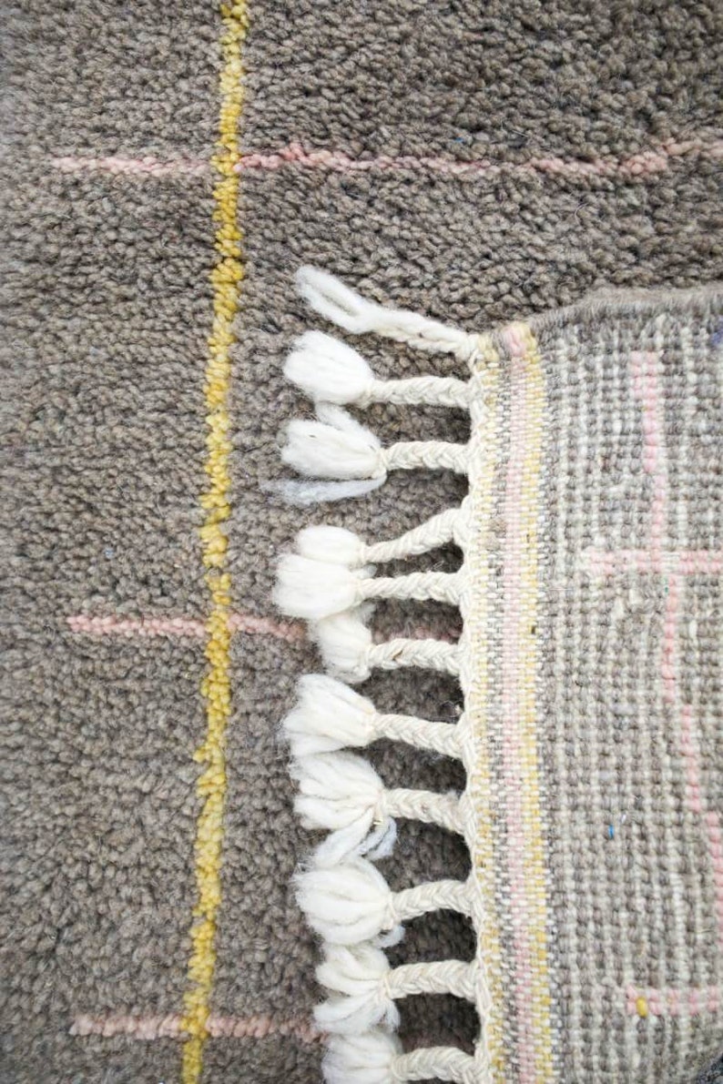 May include: Close-up of a gray and white woven rug with a fringe border. The rug has a geometric pattern with yellow and pink accents.