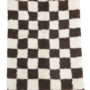 May include: A white and brown checkered rug with a fringe border. The rug is made of a soft, fluffy material.