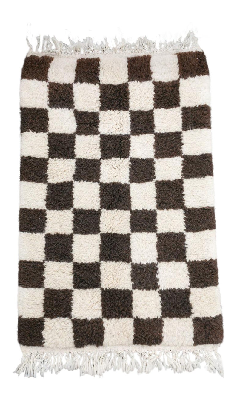 May include: A white and brown checkered rug with a fringe border. The rug is made of a soft, fluffy material.