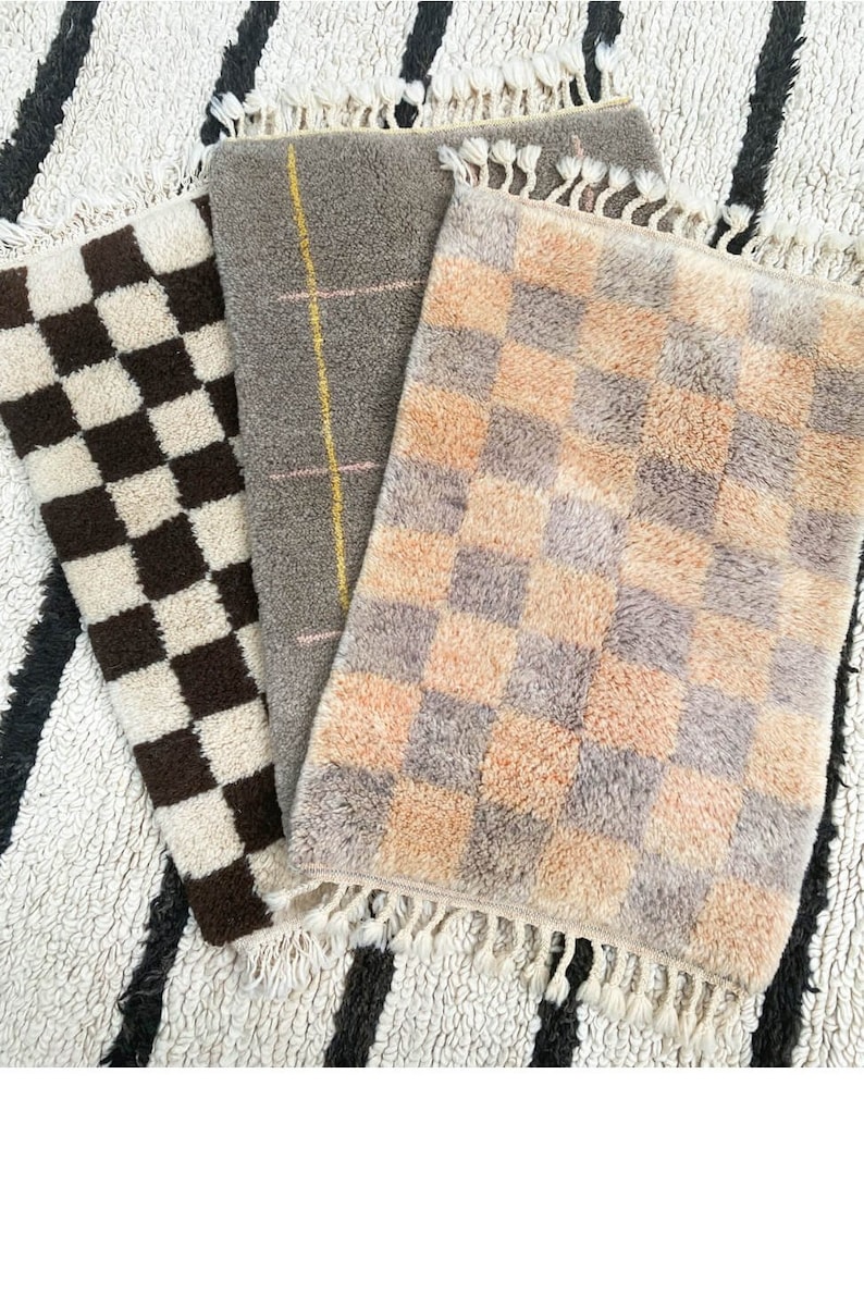 May include: Three small rugs with different patterns. The first rug is black and white checkered. The second rug is gray with a pink and yellow stripe pattern. The third rug is a light brown and peach checkered pattern.
