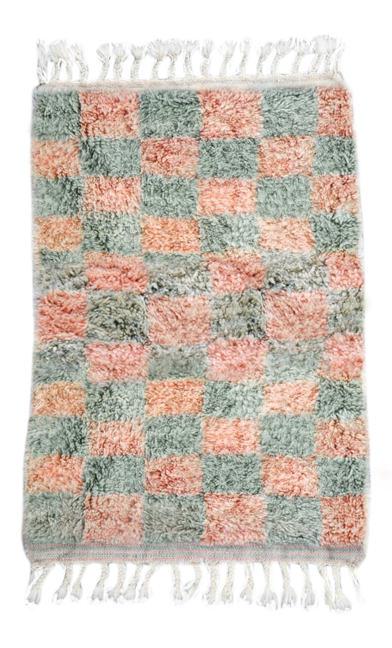 May include: A pink and green checkered rug with a fringe border. The rug is made of a soft, fluffy material.