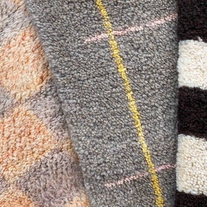 May include: Close-up of three different textured rugs. The first rug is a light brown and gray with a geometric pattern. The second rug is a gray with a yellow and pink striped pattern. The third rug is a black and white striped pattern.