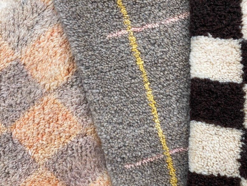 May include: Close-up of three different textured rugs. The first rug is a light brown and gray with a geometric pattern. The second rug is a gray with a yellow and pink striped pattern. The third rug is a black and white striped pattern.