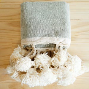 May include: A soft, gray throw blanket with a fringe border and white pom-poms.