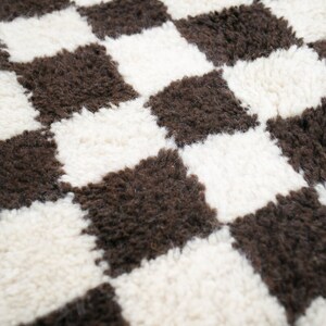 May include: A close-up of a brown and white checkered rug with a fluffy texture.