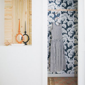 May include: A white closet door is open, revealing a closet with a blue and white floral wallpaper. A striped dress hangs on a clothes hanger inside the closet. A small rug with pink and white stripes is on the floor of the closet.