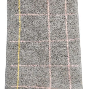 May include: A gray rug with a pink and yellow checkered pattern. The rug has a white fringe border.