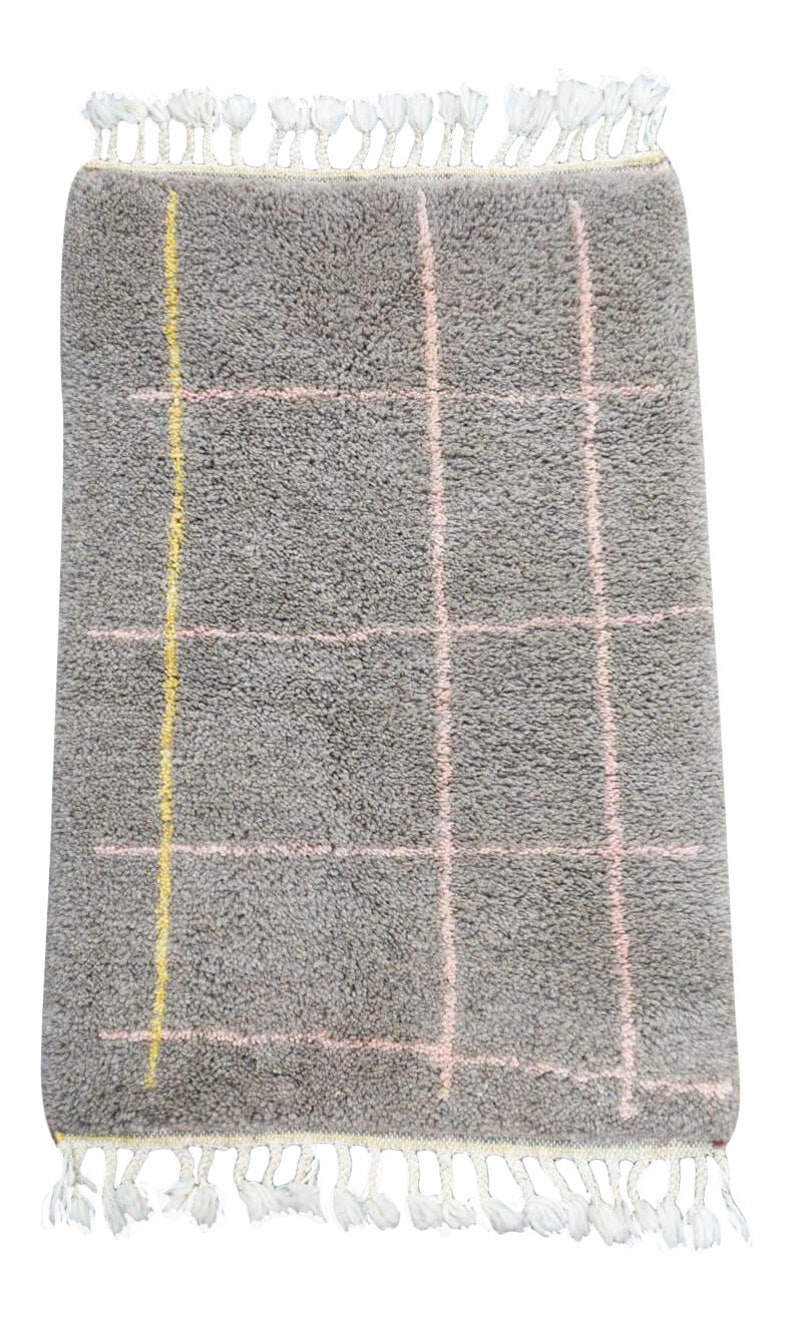 May include: A gray rug with a pink and yellow checkered pattern. The rug has a white fringe border.