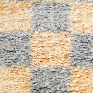 May include: Close-up of a checkered fabric with alternating squares of light brown and gray. The fabric has a fuzzy texture, resembling a plush rug or blanket.