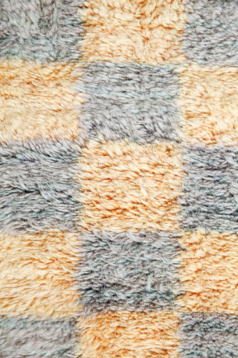 May include: Close-up of a checkered fabric with alternating squares of light brown and gray. The fabric has a fuzzy texture, resembling a plush rug or blanket.