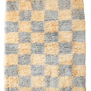 May include: A checkered rug with a light gray and yellow pattern. The rug has a fringe border.