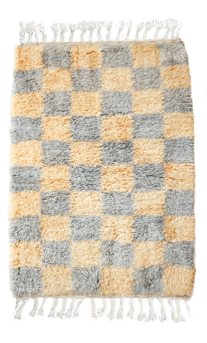 May include: A checkered rug with a light gray and yellow pattern. The rug has a fringe border.