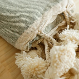 May include: A soft, green throw blanket with a white fringe and tassels. The blanket is folded and the tassels are visible.