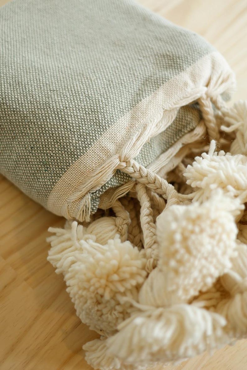 May include: A soft, green throw blanket with a white fringe and tassels. The blanket is folded and the tassels are visible.