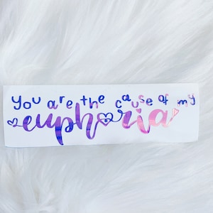 May include: A white sticker with the text "You are the cause of my euphoria" in a handwritten style. The word "euphoria" is in a gradient of pink and purple, with a heart symbol. The other words are in blue.