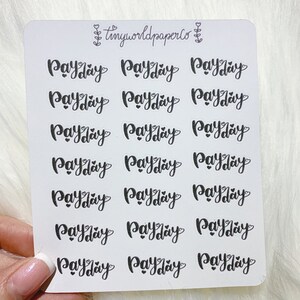 May include: A sheet of stickers featuring the word "Payday" in a handwritten style, repeated across the surface. Each instance of "Payday" has a heart replacing the letter "a". The stickers are black on white. The brand name "tinyworldpaperco" is at the top.