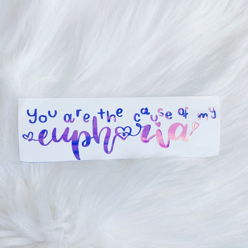 May include: A white sticker with the text "You are the cause of my euphoria" in a handwritten style. The word "euphoria" is in a gradient of pink and purple, with a heart symbol. The other words are in blue.