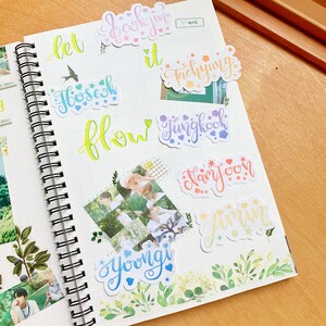 May include: A notebook with colorful handwritten names and stickers. The names include "let it flow", "Jungkook", "Jimin", "Hoseok", "Yoongi", "Namjoon", "Taehyung", and "Seokjin".