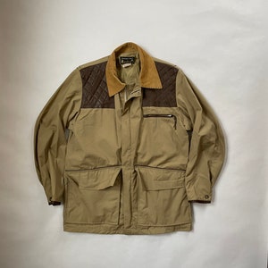 May include: A tan jacket with a brown corduroy collar and leather shoulder patches. The jacket has a zipper closure and multiple pockets.