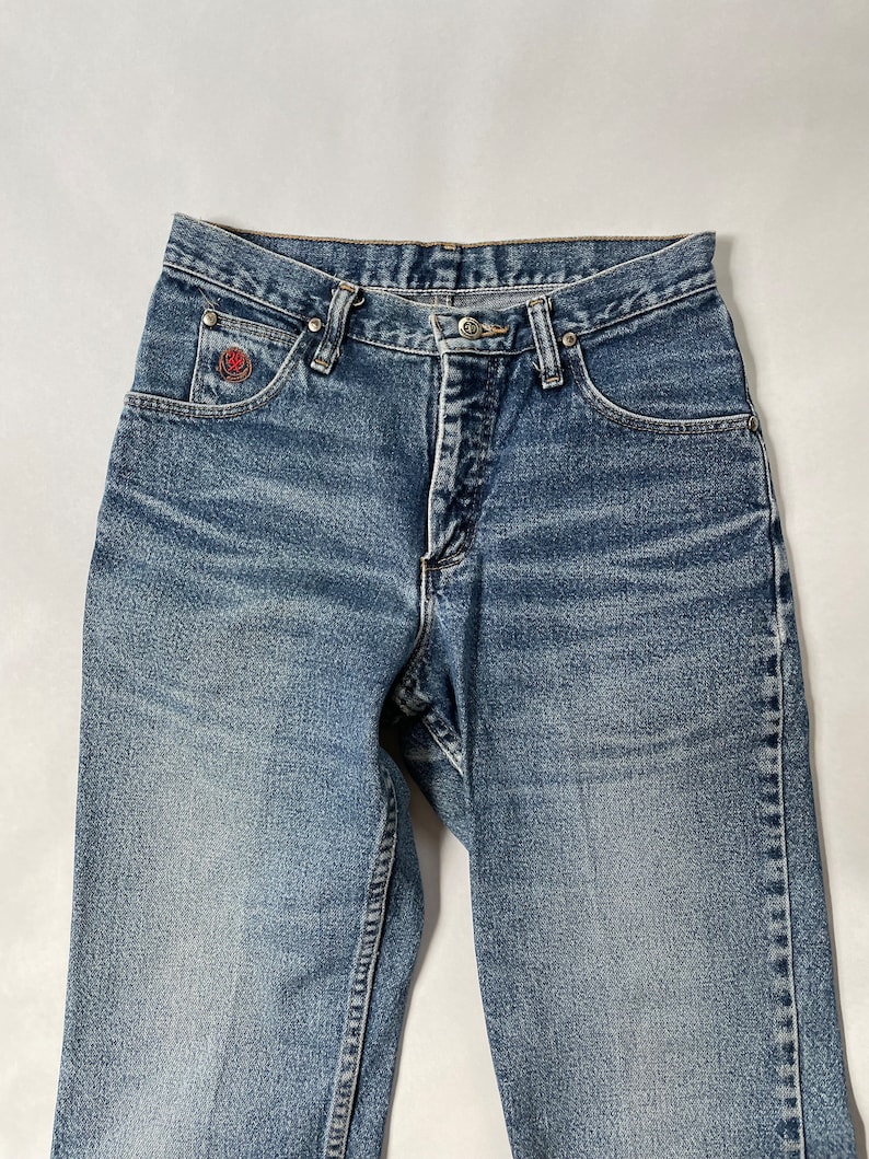 May include: A pair of light blue denim jeans with a red logo on the left pocket.