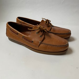 May include: A pair of brown leather boat shoes with laces. The shoes have a brown leather sole and a white background.
