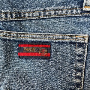 May include: Close-up of a blue denim pocket with a red, black, and gold label that reads "Twenty X".