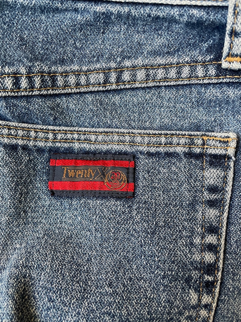 May include: Close-up of a blue denim pocket with a red, black, and gold label that reads "Twenty X".